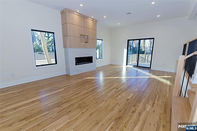 unfurnished living room with a high end fireplace, baseboards, light wood finished floors, and recessed lighting