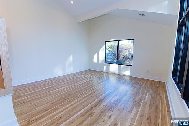 empty room featuring high vaulted ceiling, light wood-type flooring, visible vents, and baseboards