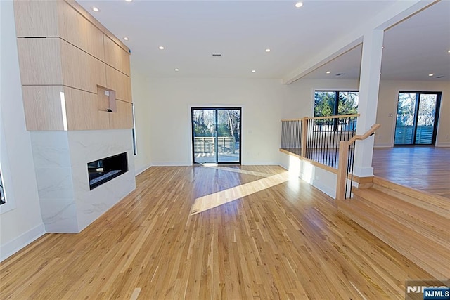 unfurnished living room featuring light wood-style floors, recessed lighting, baseboards, and a high end fireplace