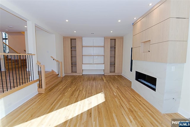 unfurnished living room featuring recessed lighting, stairway, a fireplace, and light wood-style floors