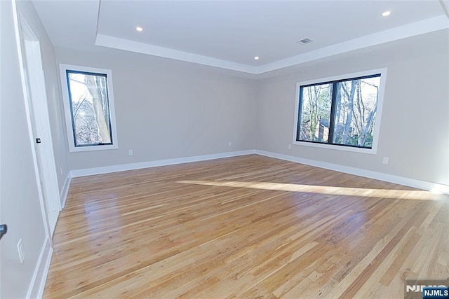 empty room featuring light wood finished floors, plenty of natural light, visible vents, and a raised ceiling