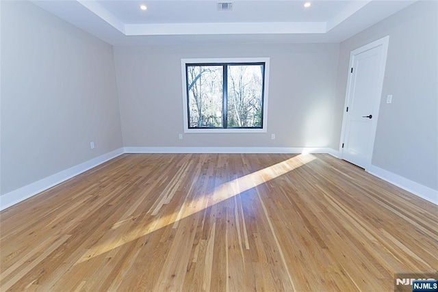 spare room featuring light wood-type flooring, a raised ceiling, and baseboards