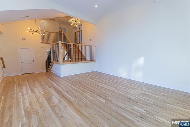 unfurnished living room with high vaulted ceiling, wood finished floors, visible vents, stairway, and an inviting chandelier