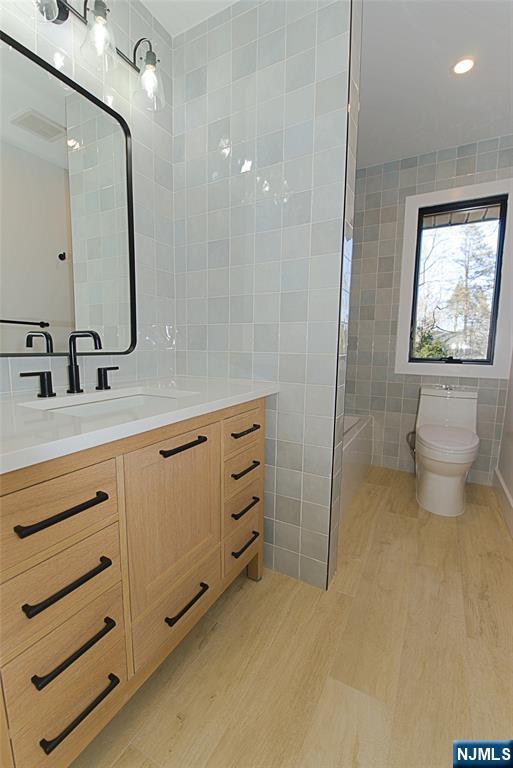 full bathroom featuring tile walls, visible vents, toilet, vanity, and wood finished floors