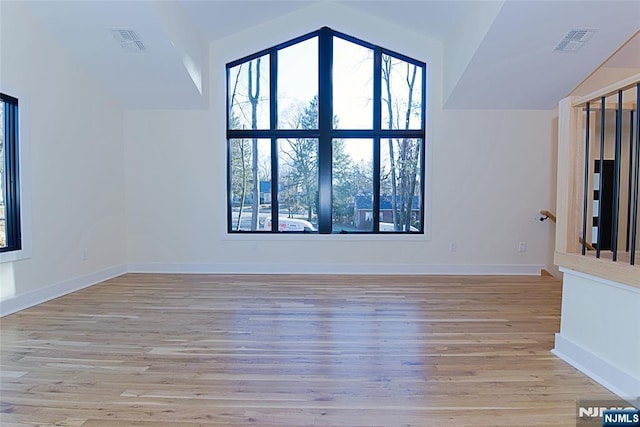 unfurnished room featuring lofted ceiling, light wood-type flooring, visible vents, and baseboards