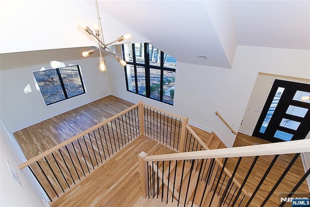 staircase featuring visible vents, vaulted ceiling, wood finished floors, and a chandelier