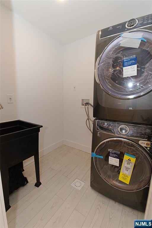 washroom with stacked washer and dryer, laundry area, baseboards, and wood finished floors