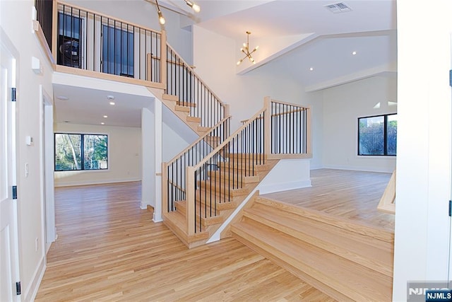 staircase with high vaulted ceiling, wood finished floors, visible vents, and a notable chandelier