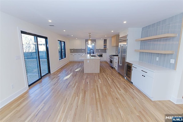 kitchen featuring premium appliances, open shelves, light countertops, light wood-style floors, and a sink