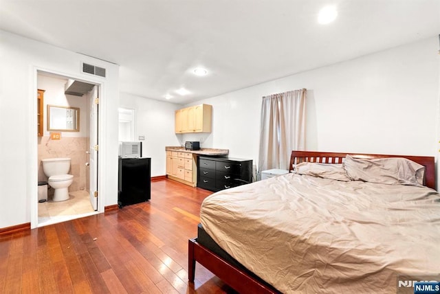 bedroom with tile walls, dark wood-type flooring, and ensuite bathroom