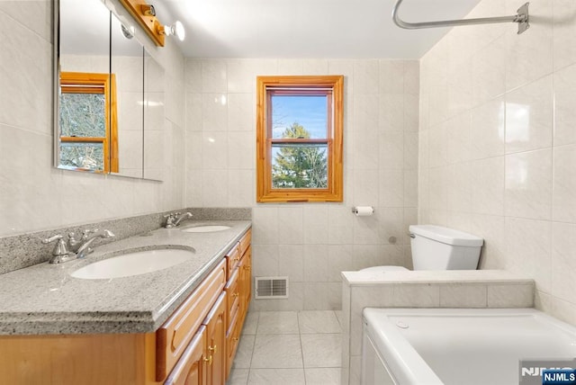 bathroom featuring tile walls, a tub to relax in, tile patterned flooring, vanity, and toilet