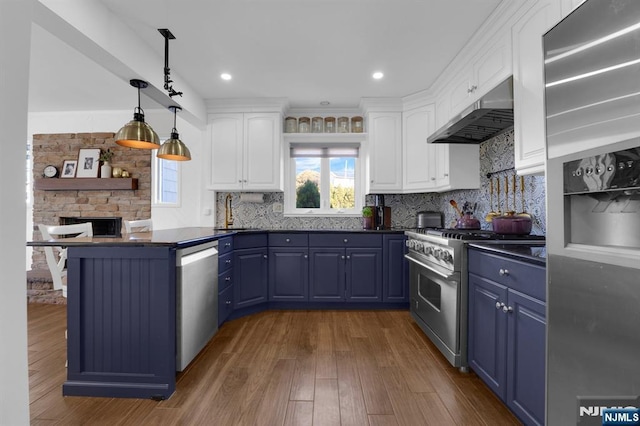 kitchen with blue cabinets, wall chimney exhaust hood, white cabinetry, pendant lighting, and stainless steel appliances