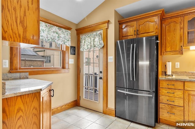 kitchen featuring vaulted ceiling, light stone countertops, light tile patterned floors, and stainless steel fridge