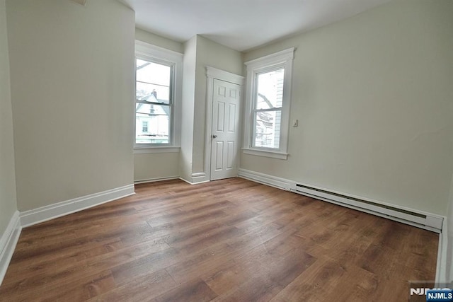 unfurnished room featuring baseboard heating, dark hardwood / wood-style floors, and a wealth of natural light