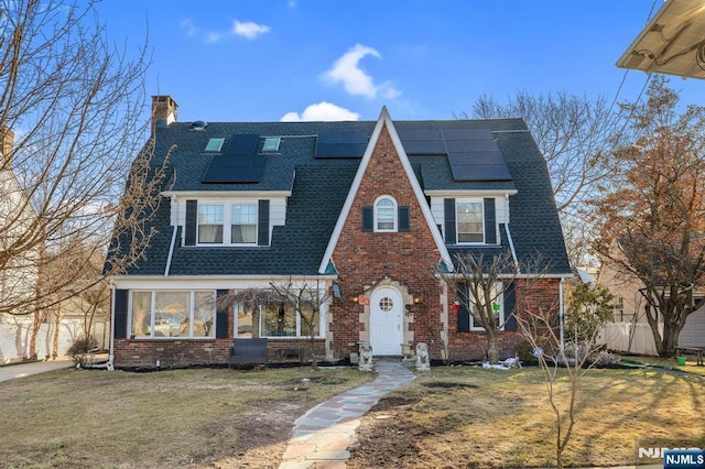 view of front of property featuring roof with shingles, a chimney, a front lawn, and brick siding