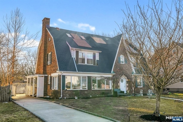 view of front facade featuring brick siding, a chimney, solar panels, a front yard, and fence