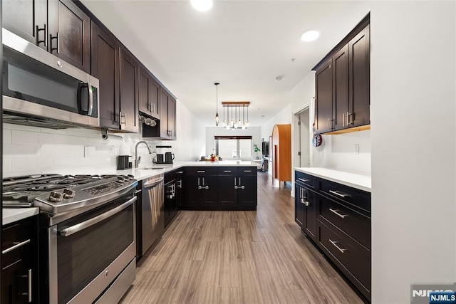 kitchen with appliances with stainless steel finishes, tasteful backsplash, sink, hanging light fixtures, and kitchen peninsula