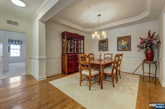 dining area featuring a raised ceiling, crown molding, hardwood / wood-style flooring, and an inviting chandelier