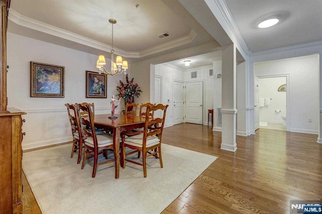 dining space with ornate columns, crown molding, an inviting chandelier, a raised ceiling, and hardwood / wood-style floors