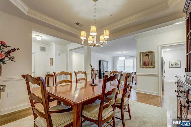 dining room featuring crown molding, a chandelier, light wood-type flooring, and a tray ceiling