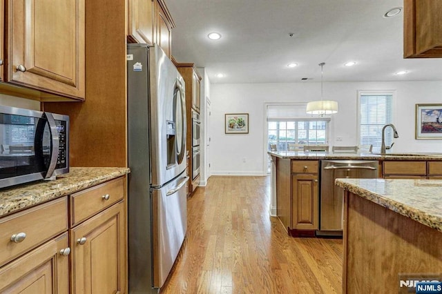 kitchen with sink, decorative light fixtures, light wood-type flooring, stainless steel appliances, and light stone countertops