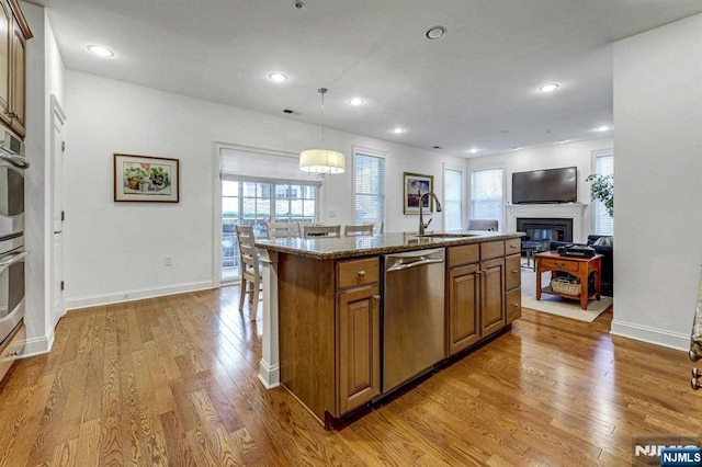 kitchen with hardwood / wood-style floors, decorative light fixtures, a kitchen island with sink, stainless steel dishwasher, and light stone countertops