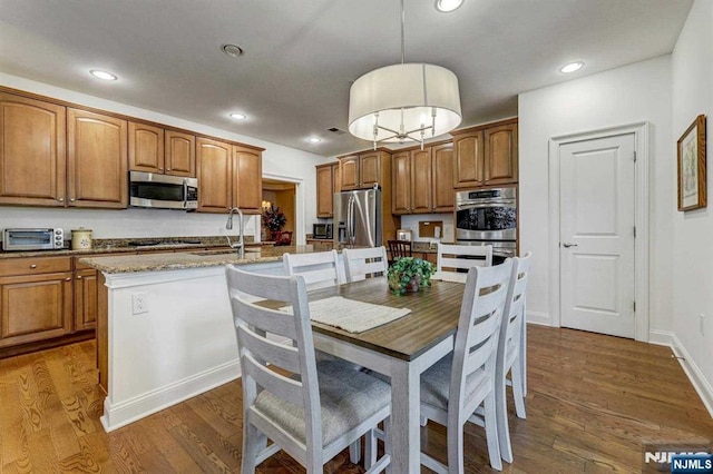 kitchen with an island with sink, sink, hanging light fixtures, black appliances, and dark wood-type flooring