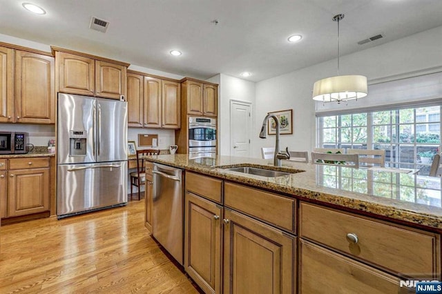 kitchen with appliances with stainless steel finishes, pendant lighting, sink, light stone counters, and light wood-type flooring