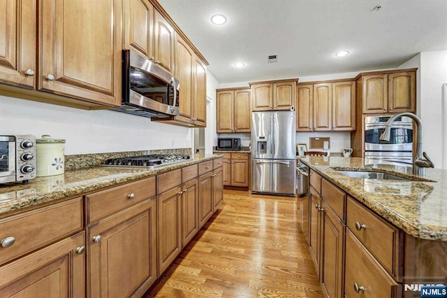 kitchen featuring sink, light hardwood / wood-style flooring, stainless steel appliances, and light stone countertops