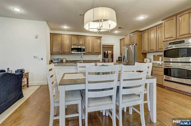 kitchen with appliances with stainless steel finishes, a kitchen island with sink, hanging light fixtures, and light wood-type flooring