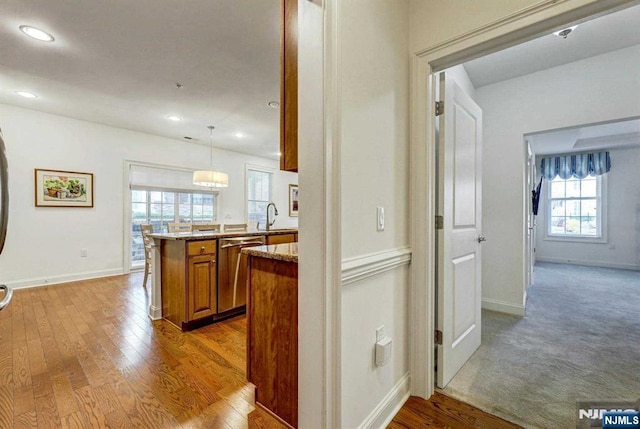 kitchen featuring pendant lighting, dishwasher, sink, kitchen peninsula, and light wood-type flooring