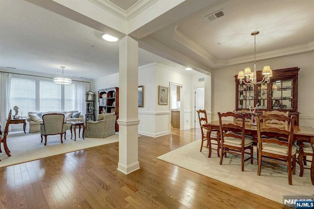 dining room featuring hardwood / wood-style flooring, ornamental molding, a chandelier, and decorative columns