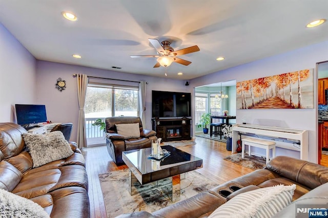 living room with ceiling fan with notable chandelier and light wood-type flooring