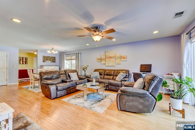 living room featuring ceiling fan with notable chandelier and light hardwood / wood-style flooring