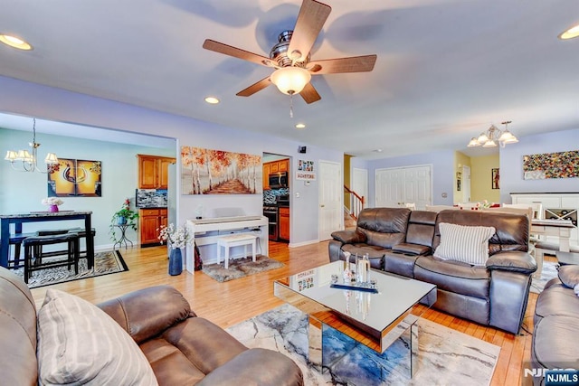 living room featuring ceiling fan with notable chandelier and light hardwood / wood-style flooring