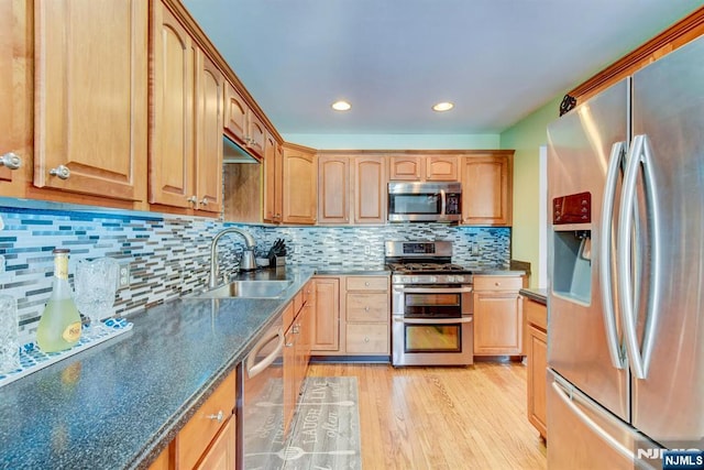 kitchen with sink, dark stone countertops, light wood-type flooring, appliances with stainless steel finishes, and decorative backsplash