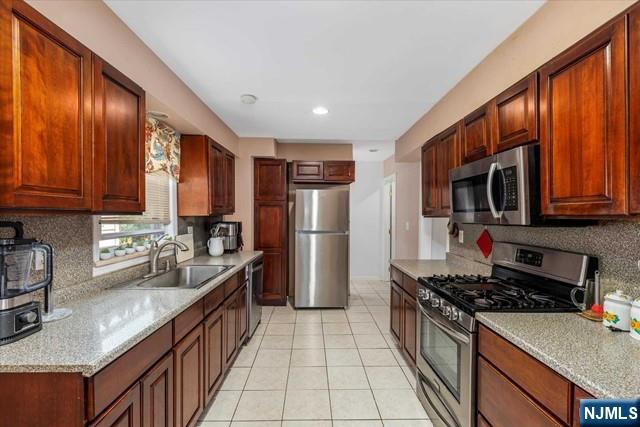 kitchen featuring appliances with stainless steel finishes, sink, decorative backsplash, light tile patterned floors, and light stone countertops