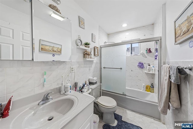 full bathroom with shower / bath combination with glass door, tile walls, vanity, tile patterned floors, and toilet