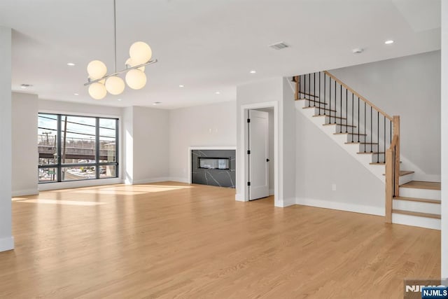 unfurnished living room featuring light hardwood / wood-style floors, a chandelier, and a high end fireplace