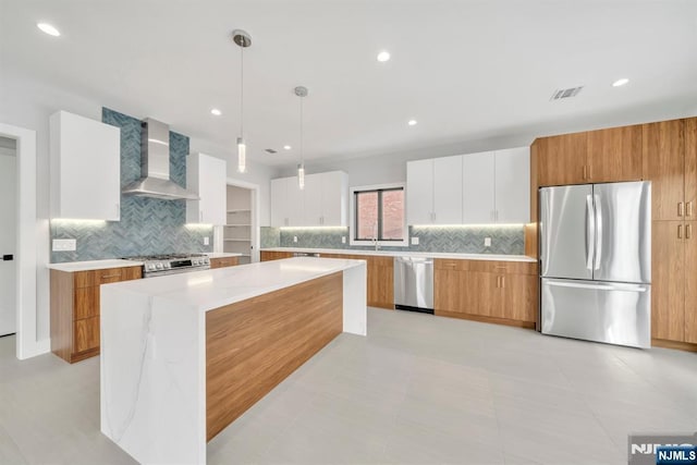 kitchen featuring hanging light fixtures, stainless steel appliances, wall chimney range hood, backsplash, and white cabinetry