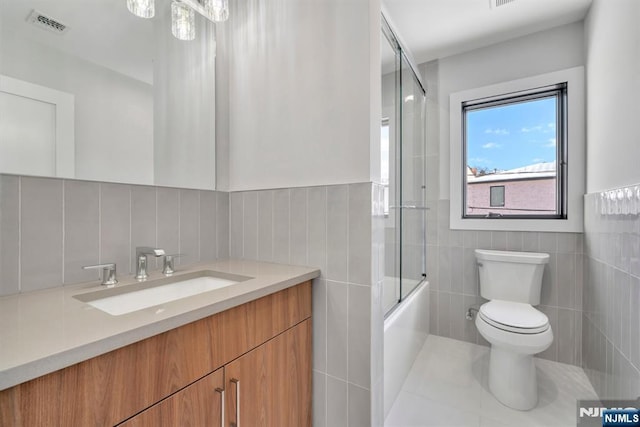 full bathroom with bath / shower combo with glass door, vanity, tile walls, and toilet