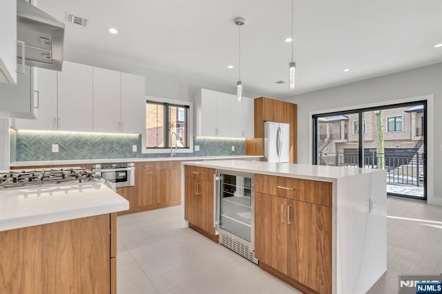 kitchen featuring a kitchen island, hanging light fixtures, white cabinets, and wine cooler