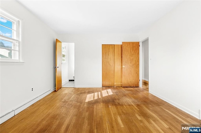 unfurnished bedroom featuring a baseboard radiator, baseboards, a closet, and light wood-style flooring