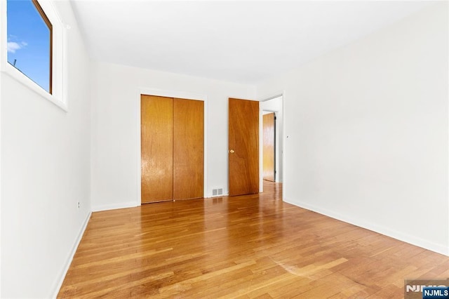 unfurnished bedroom with light wood finished floors, visible vents, baseboards, and a closet