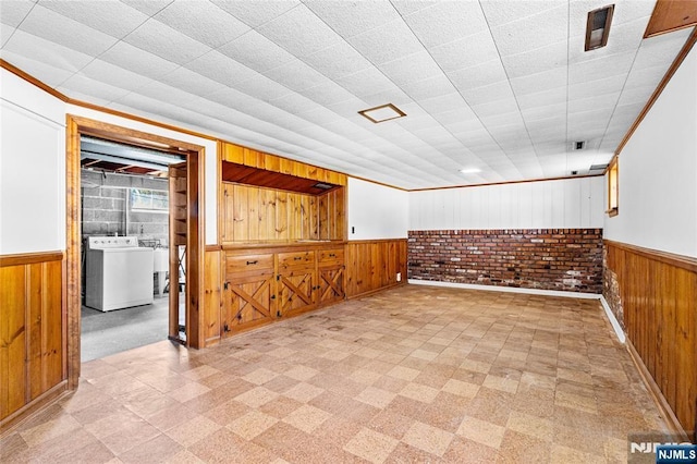 spare room featuring a wainscoted wall, washer / clothes dryer, wood walls, crown molding, and light floors