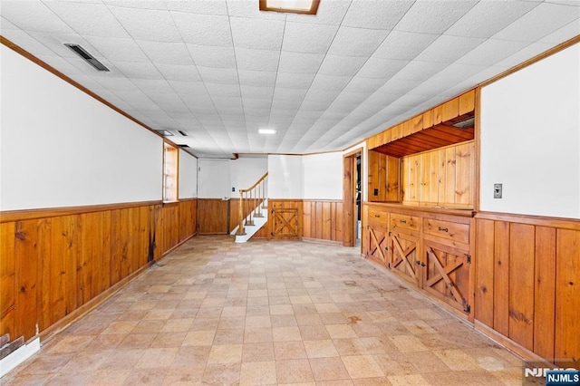 finished basement with visible vents, wainscoting, stairs, and wood walls