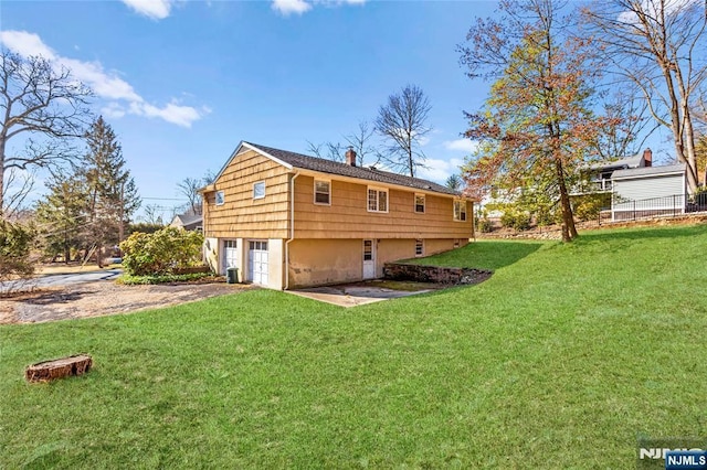 rear view of house featuring an attached garage, a lawn, driveway, and a chimney