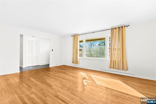 empty room featuring wood finished floors, baseboards, and baseboard heating