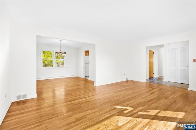 empty room featuring a notable chandelier, light wood-style floors, and visible vents