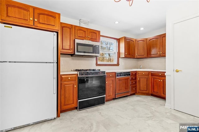 kitchen with stainless steel microwave, freestanding refrigerator, brown cabinetry, light countertops, and black range with gas stovetop